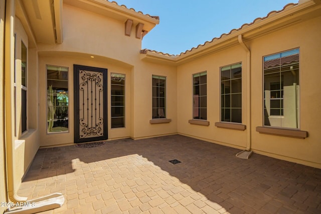 entrance to property featuring a patio, stucco siding, and a tiled roof