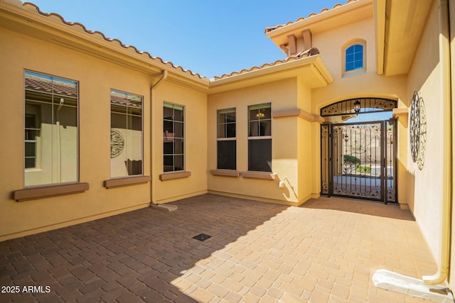 property entrance with stucco siding, a gate, a patio, and a tiled roof