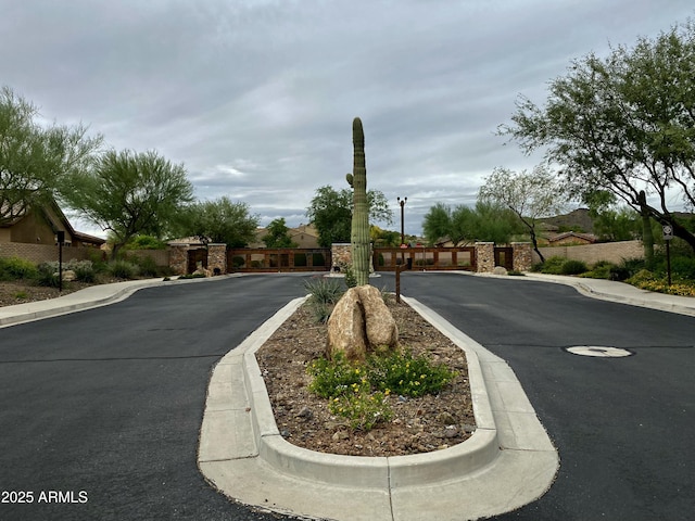 view of asphalt street featuring curbs, sidewalks, a gated entry, and street lighting