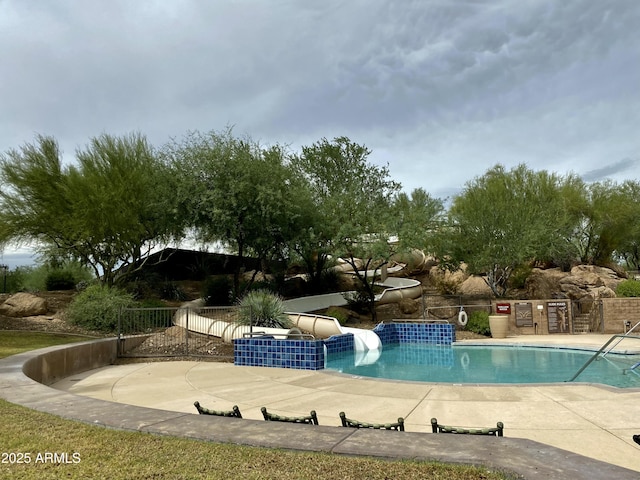 community pool featuring a water slide, fence, and a patio area