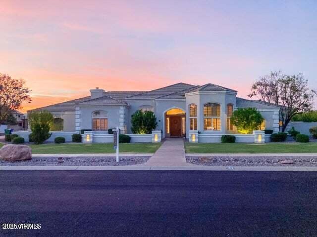 mediterranean / spanish house with a tile roof, stucco siding, a yard, and a chimney