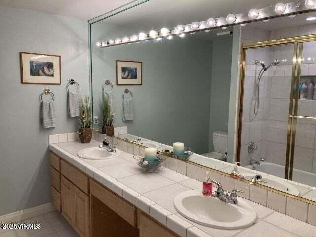 bathroom with double vanity, toilet, baseboards, and a sink