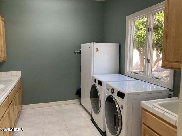 washroom featuring light tile patterned floors, baseboards, washing machine and dryer, and cabinet space