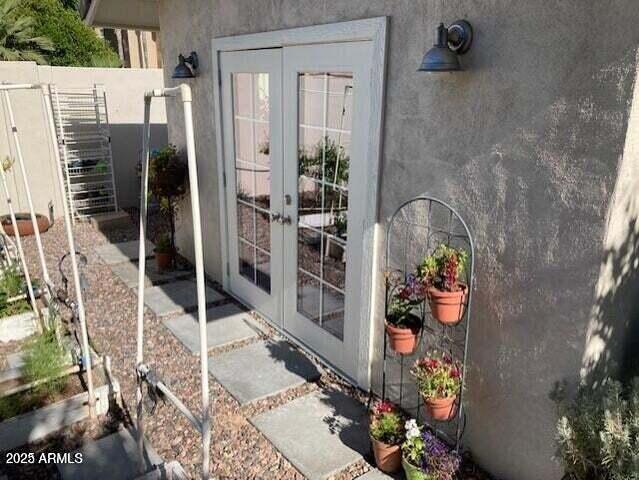 view of exterior entry featuring french doors, fence, and stucco siding