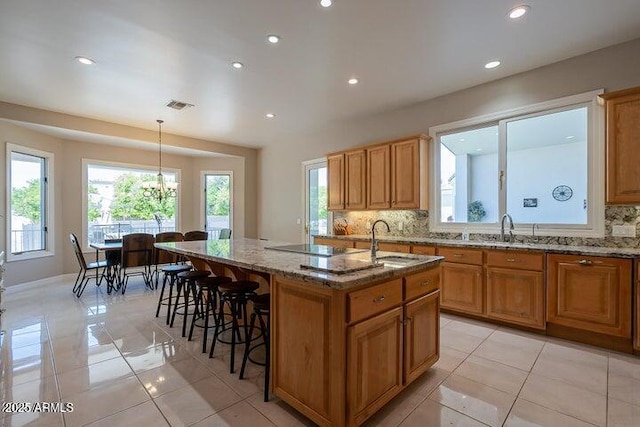 kitchen featuring stone countertops, tasteful backsplash, visible vents, and a center island with sink