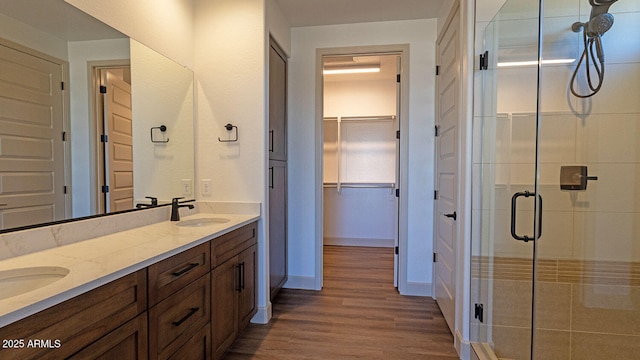 bathroom featuring a spacious closet, wood finished floors, a stall shower, and a sink