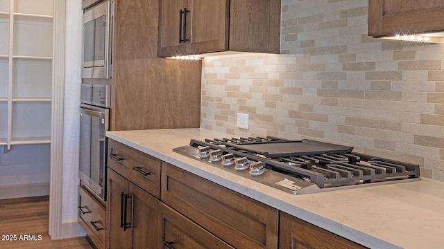 kitchen with wood finished floors, brown cabinets, light countertops, appliances with stainless steel finishes, and tasteful backsplash