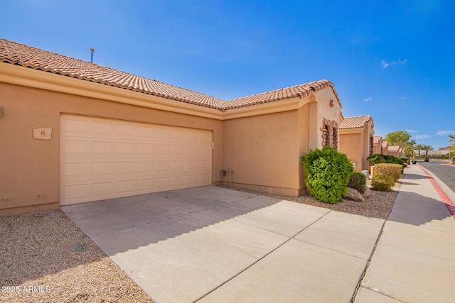 view of front of home featuring driveway, an attached garage, a tile roof, and stucco siding