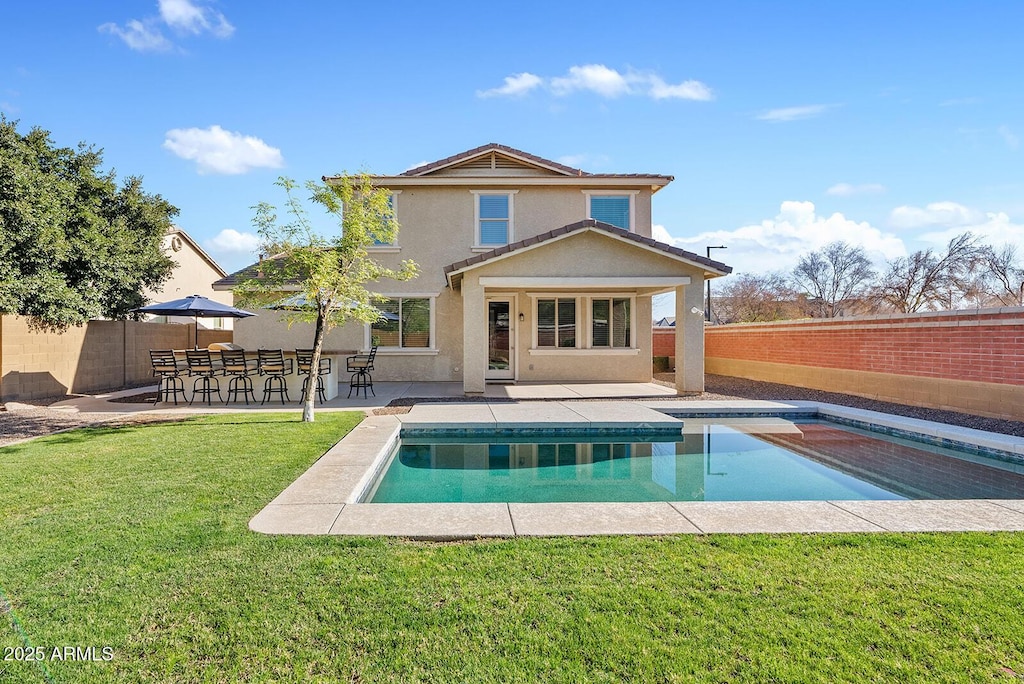 rear view of house with exterior bar, a patio, a fenced in pool, and a lawn