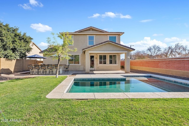 rear view of house with exterior bar, a patio, a fenced in pool, and a lawn