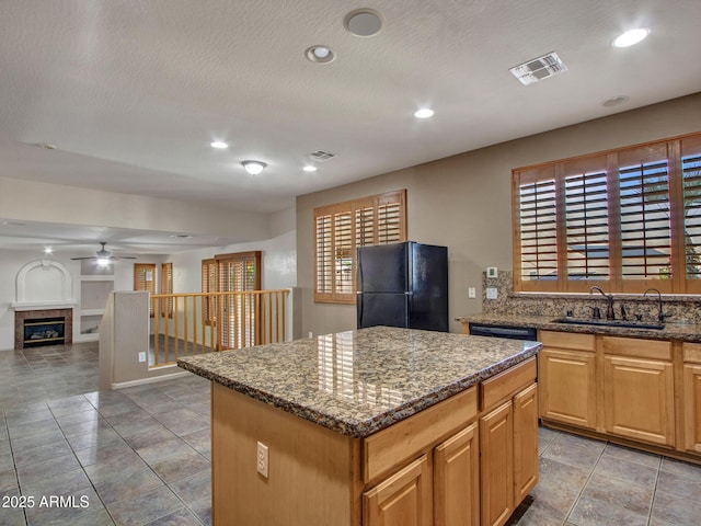 kitchen featuring a kitchen island, a sink, visible vents, freestanding refrigerator, and ceiling fan