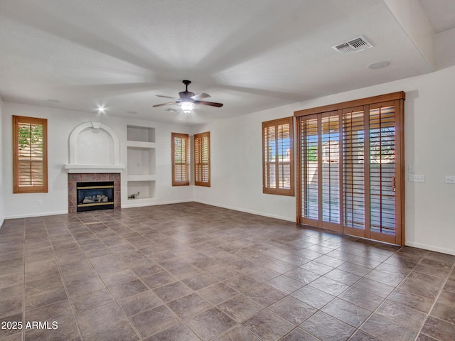 unfurnished living room featuring visible vents, baseboards, built in shelves, a tiled fireplace, and a ceiling fan