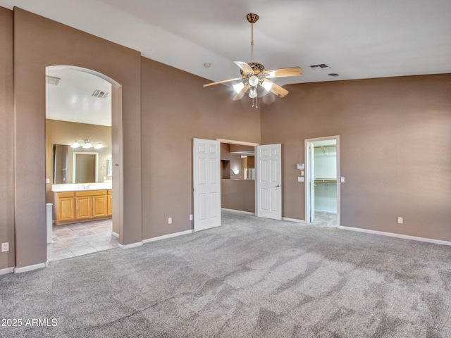 unfurnished bedroom featuring light colored carpet, visible vents, high vaulted ceiling, and arched walkways