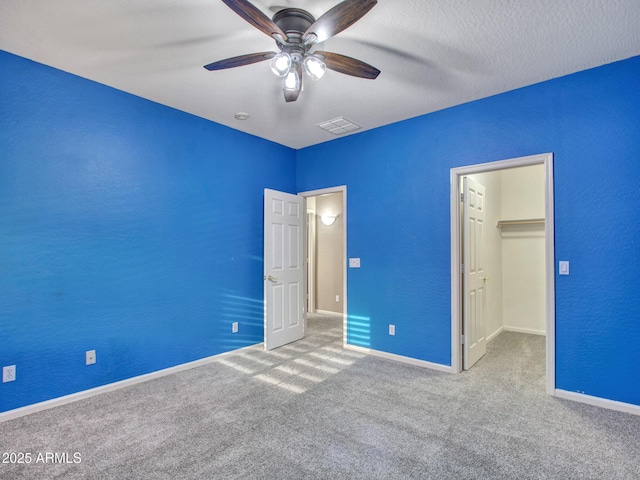 unfurnished bedroom with a closet, a ceiling fan, a spacious closet, visible vents, and carpet