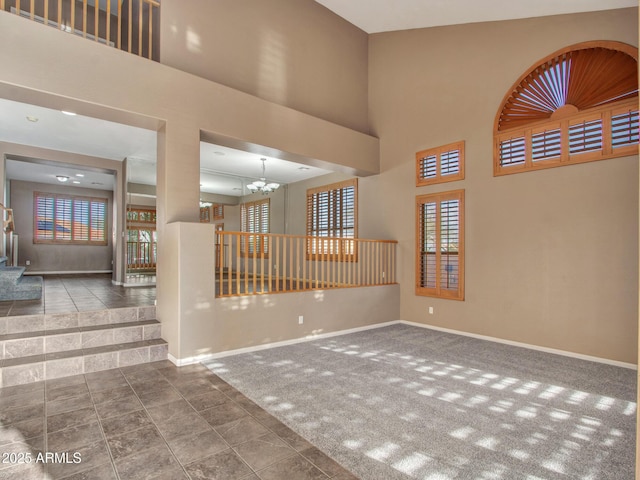 unfurnished room with carpet flooring, a towering ceiling, a notable chandelier, and baseboards