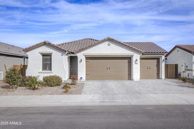 mediterranean / spanish-style house featuring a garage, a tiled roof, decorative driveway, and stucco siding