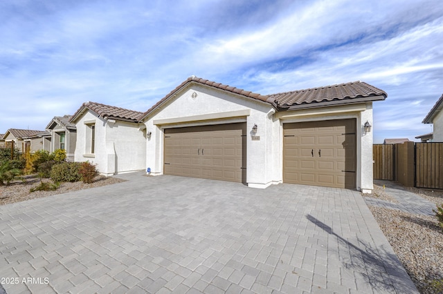 mediterranean / spanish house featuring decorative driveway, fence, an attached garage, and stucco siding