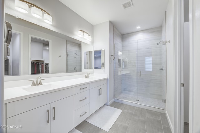 full bathroom with visible vents, a sink, a shower stall, and double vanity