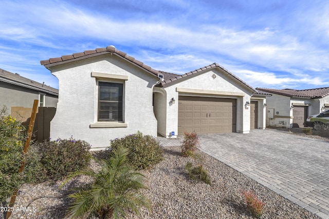 mediterranean / spanish-style house with a garage, decorative driveway, a tile roof, and stucco siding