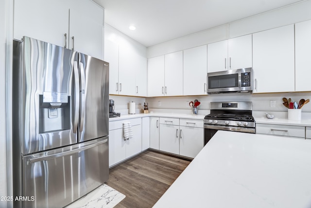 kitchen with appliances with stainless steel finishes, dark wood-style flooring, light countertops, and white cabinets