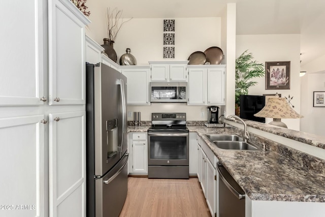 kitchen with dark stone countertops, sink, light wood-type flooring, appliances with stainless steel finishes, and white cabinets