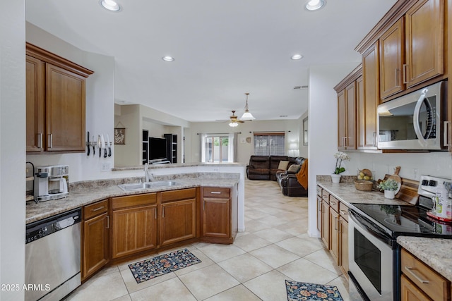 kitchen with brown cabinetry, appliances with stainless steel finishes, open floor plan, a peninsula, and a sink