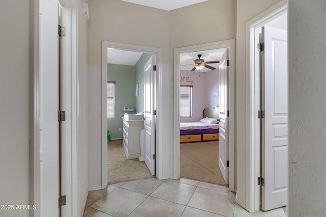 hall with light carpet, baseboards, and light tile patterned floors