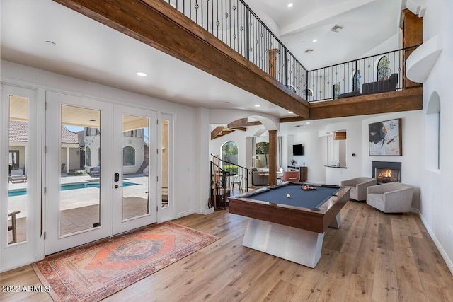 rec room featuring arched walkways, a warm lit fireplace, pool table, and wood finished floors