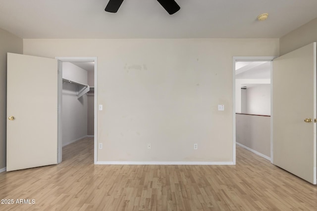 unfurnished bedroom featuring a closet, a spacious closet, light wood-type flooring, ceiling fan, and baseboards