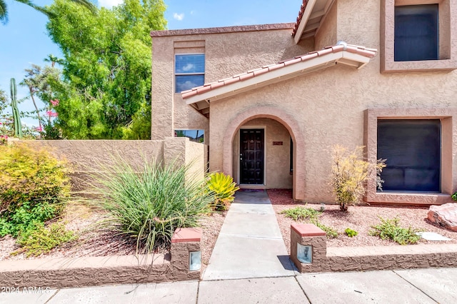 property entrance featuring a tiled roof, fence, and stucco siding