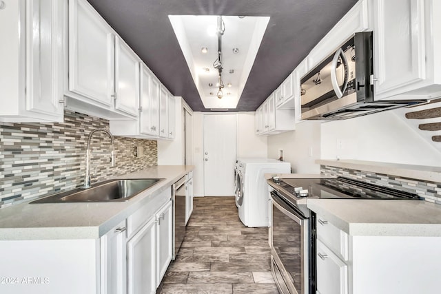 kitchen featuring a sink, washing machine and dryer, appliances with stainless steel finishes, white cabinets, and a tray ceiling