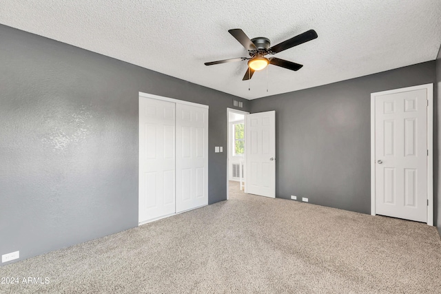 unfurnished bedroom with a textured wall, carpet, ceiling fan, a textured ceiling, and a closet