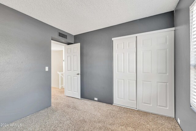 unfurnished bedroom with light carpet, visible vents, a textured ceiling, a textured wall, and a closet