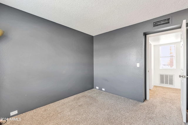 spare room with visible vents, light colored carpet, and a textured ceiling