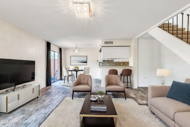 living room featuring a textured ceiling, stairs, light wood finished floors, and visible vents