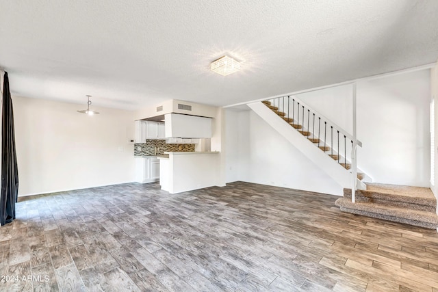 unfurnished living room featuring stairs, wood finished floors, and a textured ceiling