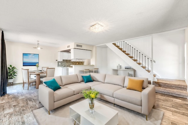 living area with light wood-type flooring, stairs, and a textured ceiling