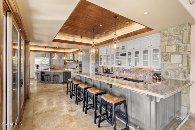 kitchen featuring a tray ceiling, wall chimney range hood, a breakfast bar, and decorative light fixtures