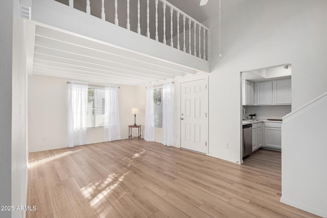 unfurnished living room featuring light wood-type flooring and a towering ceiling