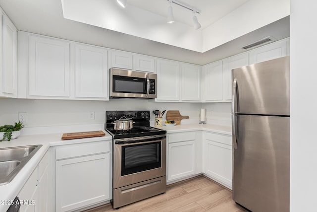 kitchen with rail lighting, white cabinetry, and stainless steel appliances