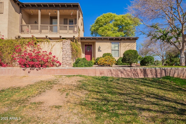 view of front of property with stucco siding, a balcony, and a front yard