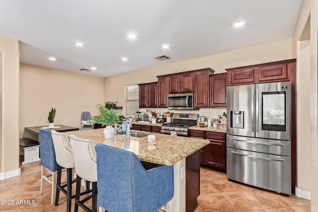 kitchen featuring visible vents, light stone countertops, a center island with sink, a kitchen breakfast bar, and stainless steel appliances