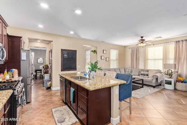 kitchen featuring a breakfast bar, an island with sink, light tile patterned flooring, stainless steel appliances, and a sink