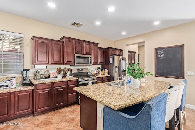 kitchen featuring visible vents, a center island with sink, a kitchen breakfast bar, stainless steel appliances, and a sink