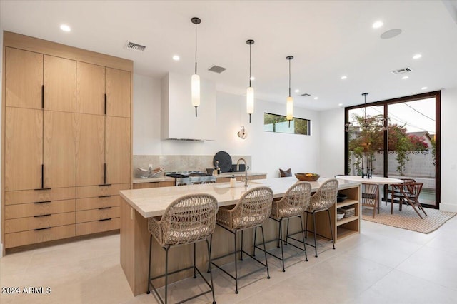 kitchen featuring decorative light fixtures, backsplash, a center island with sink, stove, and light tile floors