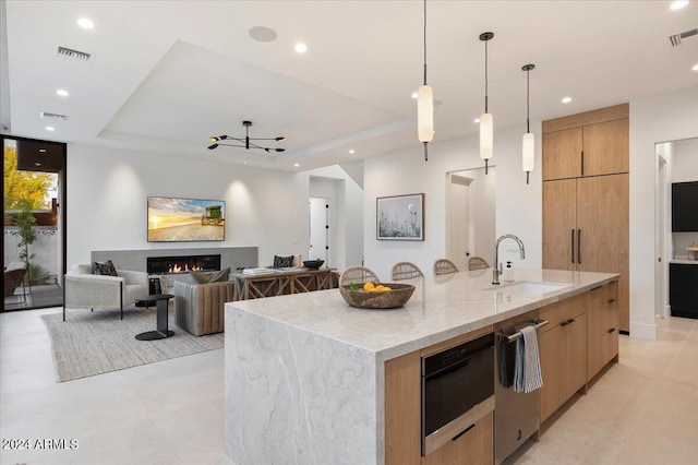 kitchen featuring light stone countertops, decorative light fixtures, dishwasher, a large island, and sink