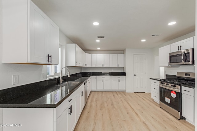 kitchen with dark stone counters, white cabinets, sink, appliances with stainless steel finishes, and light hardwood / wood-style floors