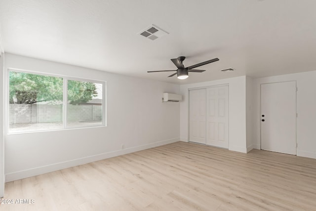 unfurnished bedroom with a wall unit AC, ceiling fan, a closet, and light wood-type flooring