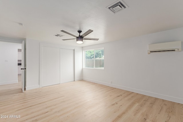 unfurnished bedroom with a wall mounted AC, light wood-type flooring, a closet, and ceiling fan