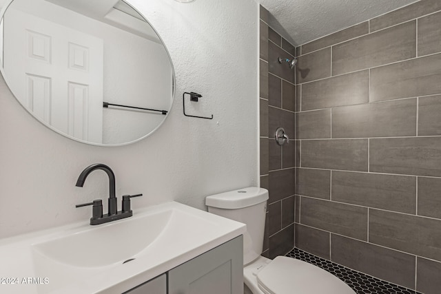 bathroom with a tile shower, vanity, a textured ceiling, and toilet